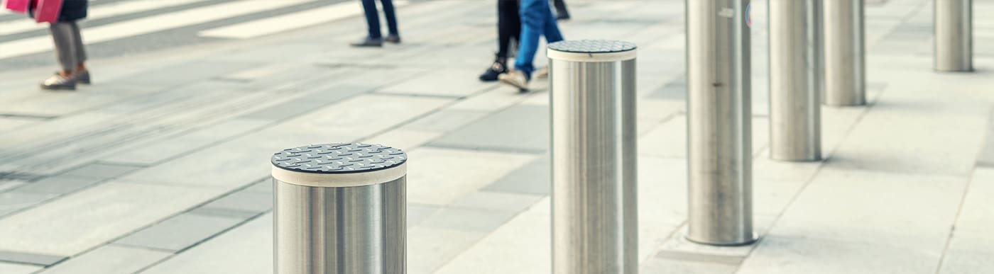 Grey stone street with peoples feet walking and six silver bollards.