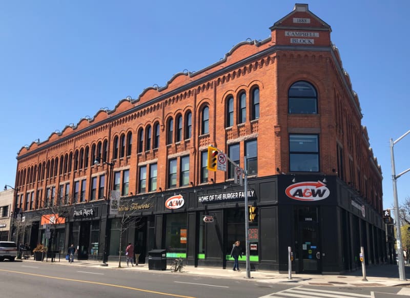 Black and red brick building on a street corner with A&W logo on the exterior.