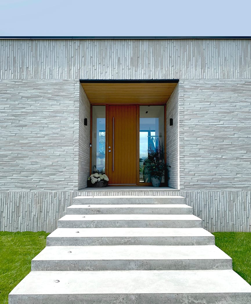 Exterior of a residential home with light grey brick, grey stone steps and a wood front door.