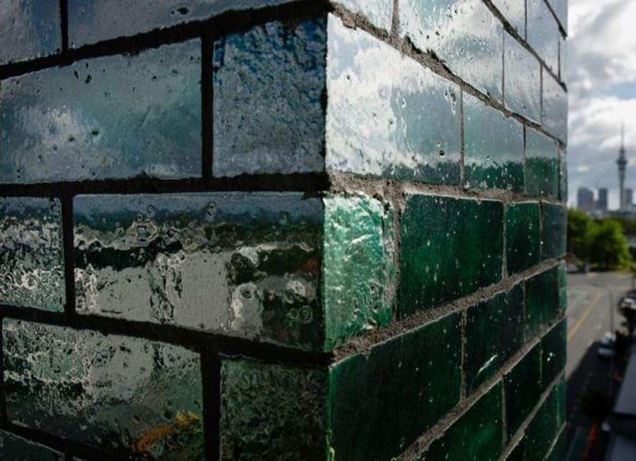 Corner view of a dark green glazed brick building with the Toronto skyline in the background..