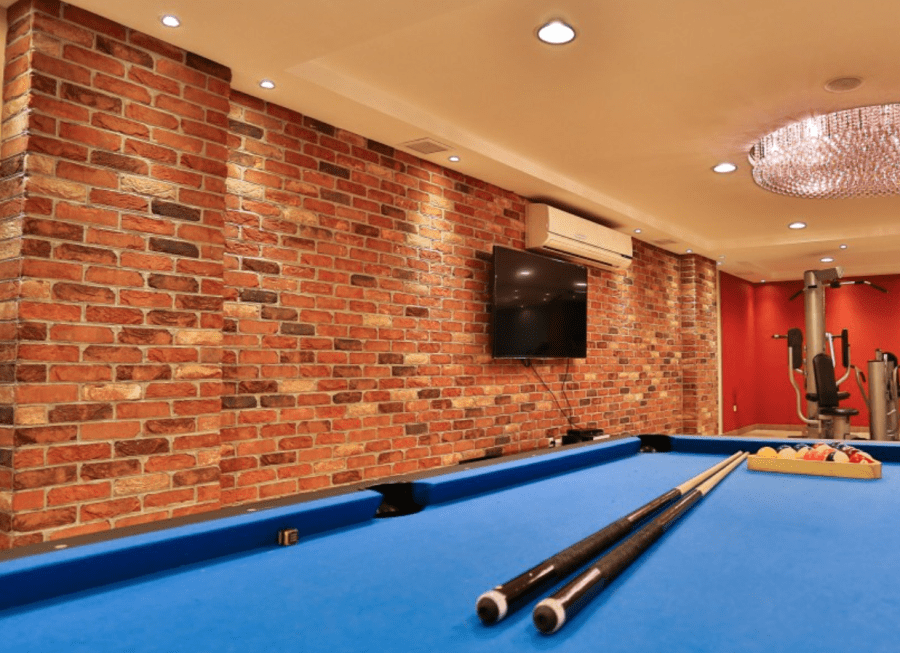 Interior wall with red brick and a pool table and gym equipment.