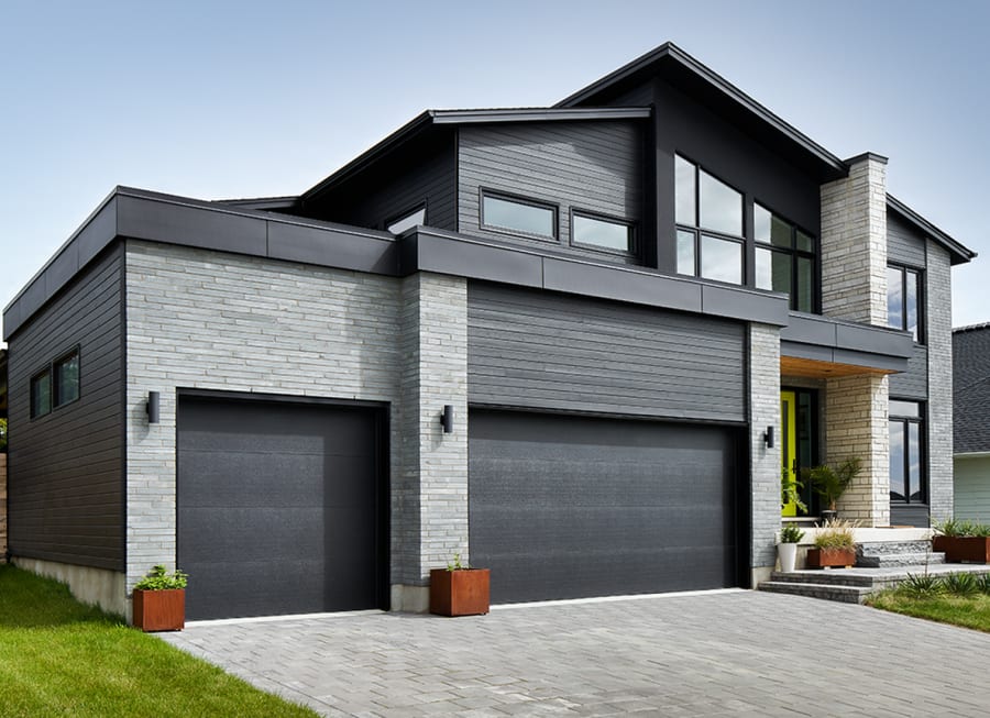 Exterior of a grey brick house with two garage doors.