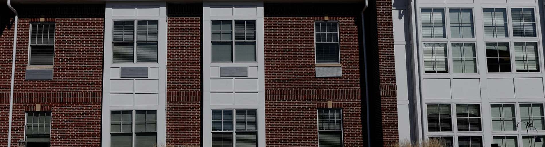 Close up of red brick building exterior with white windows, with white building to the right.