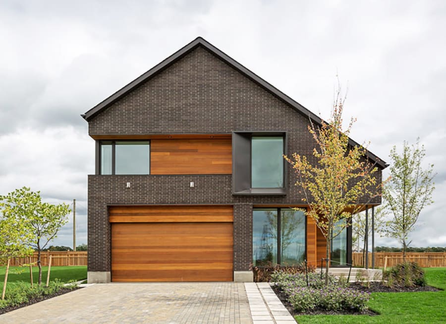 Exterior of modern home with dark grey brick and a large wood garage door.