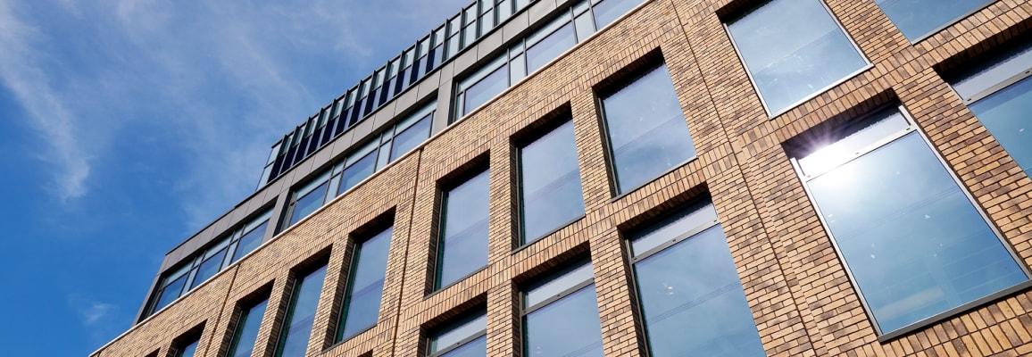 Exterior of multi-floor building with dark beige brick and large windows.