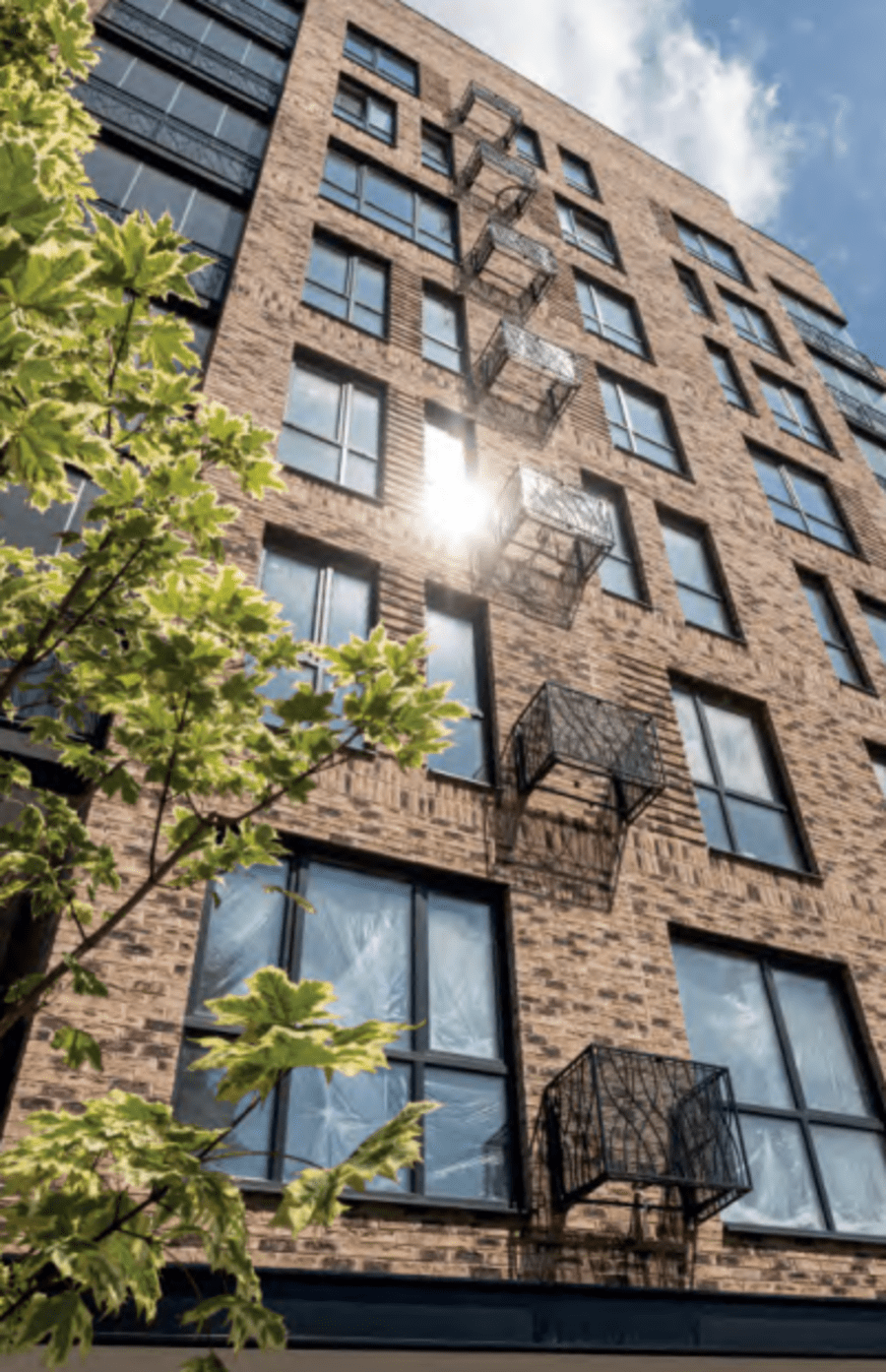 Multi-floor building with beige brick and multiple windows and a fire escape.