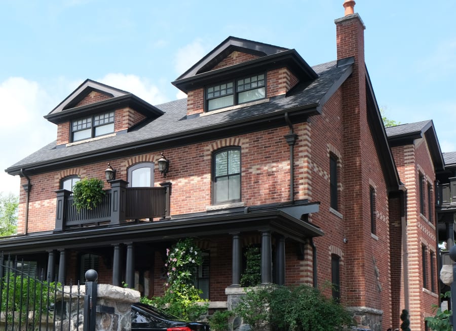 Red brick two story house with balcony and black pillars.