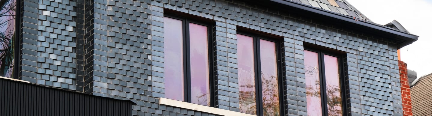 Close up of dark grey building exterior with three windows.