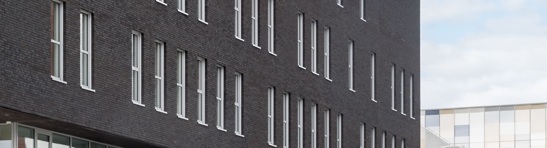 Exterior of multilevel dark grey building with many white windows.