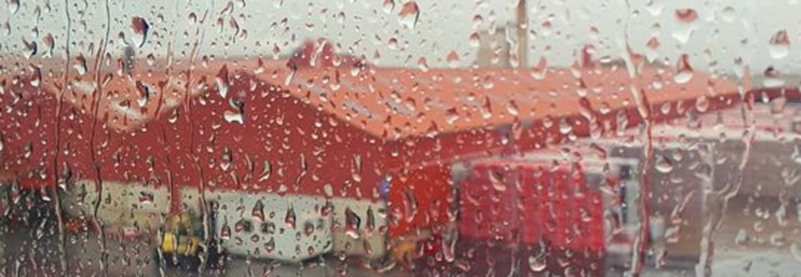 Window with rain and a blurred red building in the background.