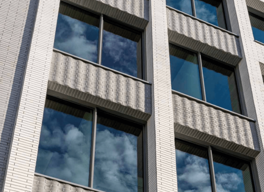 Patterned light grey brick on the exterior of a multi-floor building with large windows.