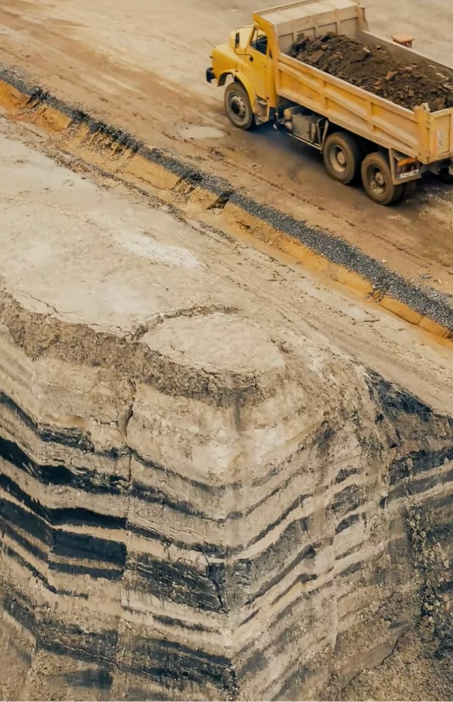 Dump truck carrying brick material on a dirt road next to a quarry.