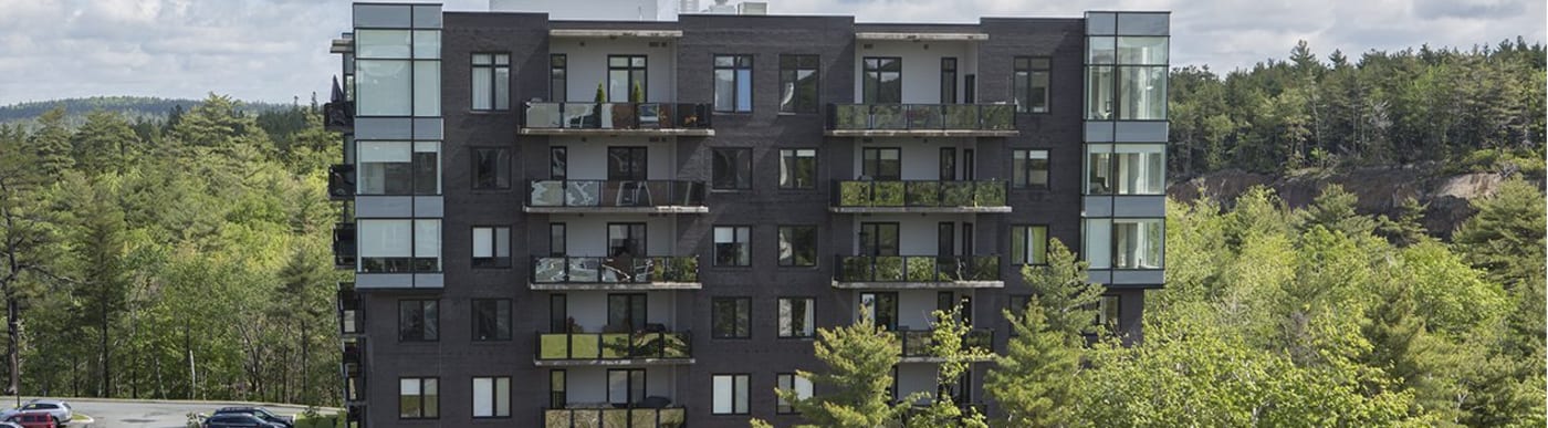 Dark grey brick residential building with balconies, surrounded by trees.