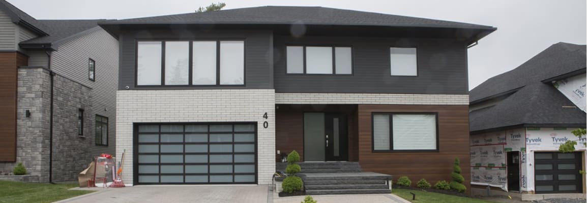 Two story modern home with grey brick on the top floor, beige brick on the garage and wood paneling. 