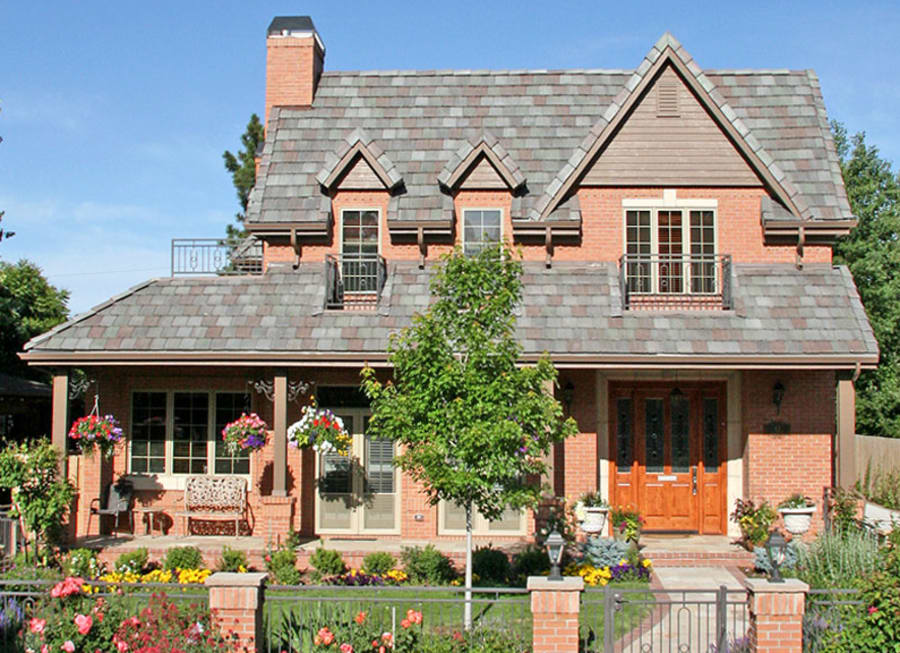 Two story residential home with red brick and lots of flowers on the lawn.