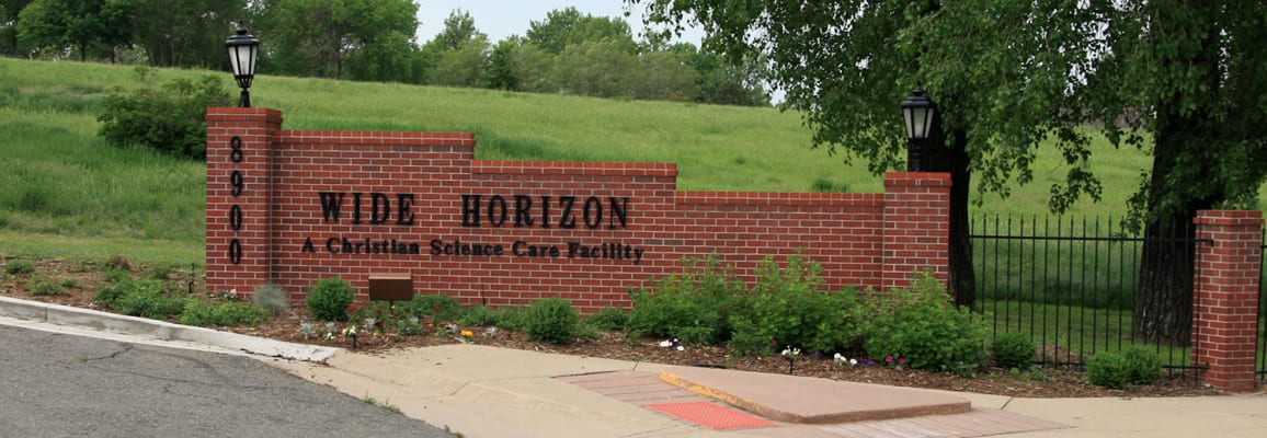 Brick wall attached to a fence with the text 'Wide Horizon A christian Science Care Facility'.