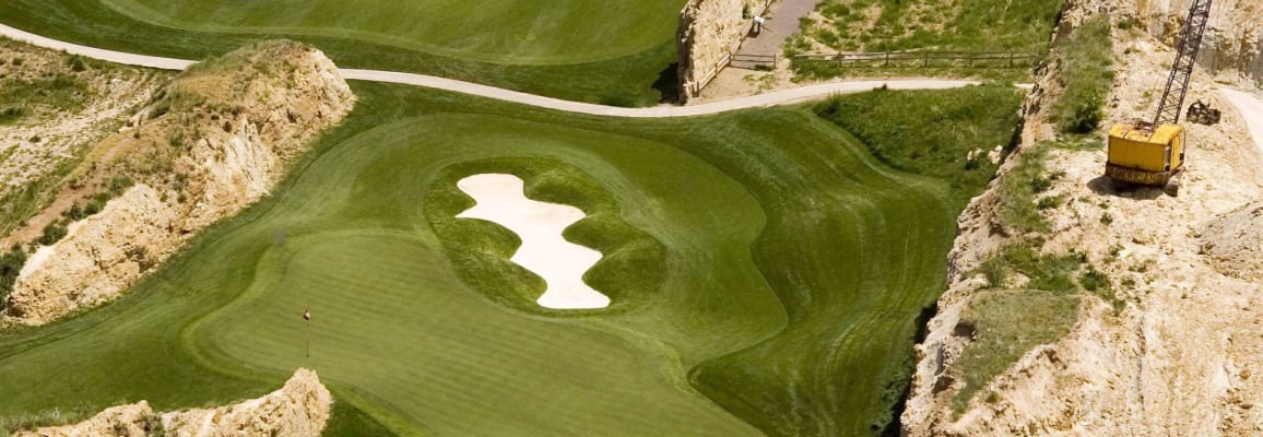 Arial view of a golf course surrounded by dirt mounds, one of which has a crane on it.