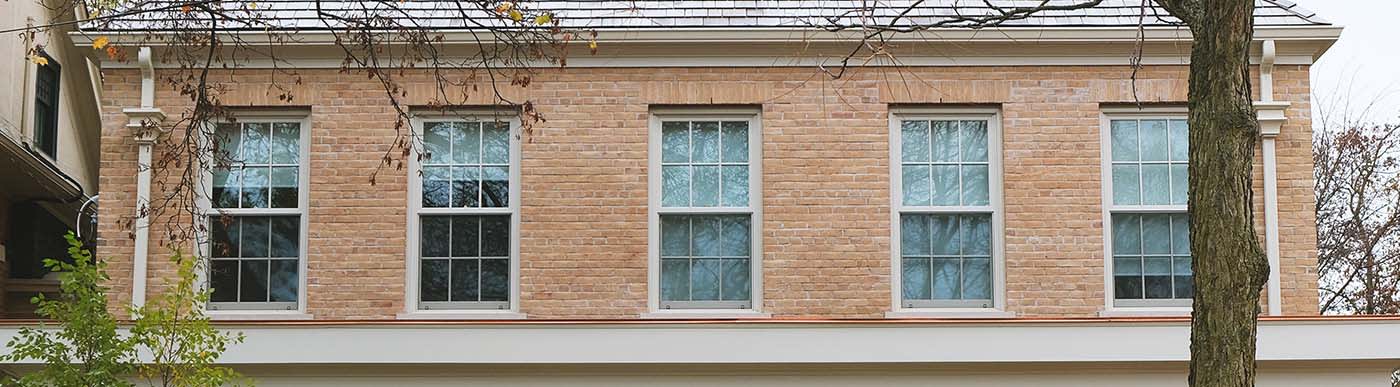 Top level of a light red brick building with 5 white windows.