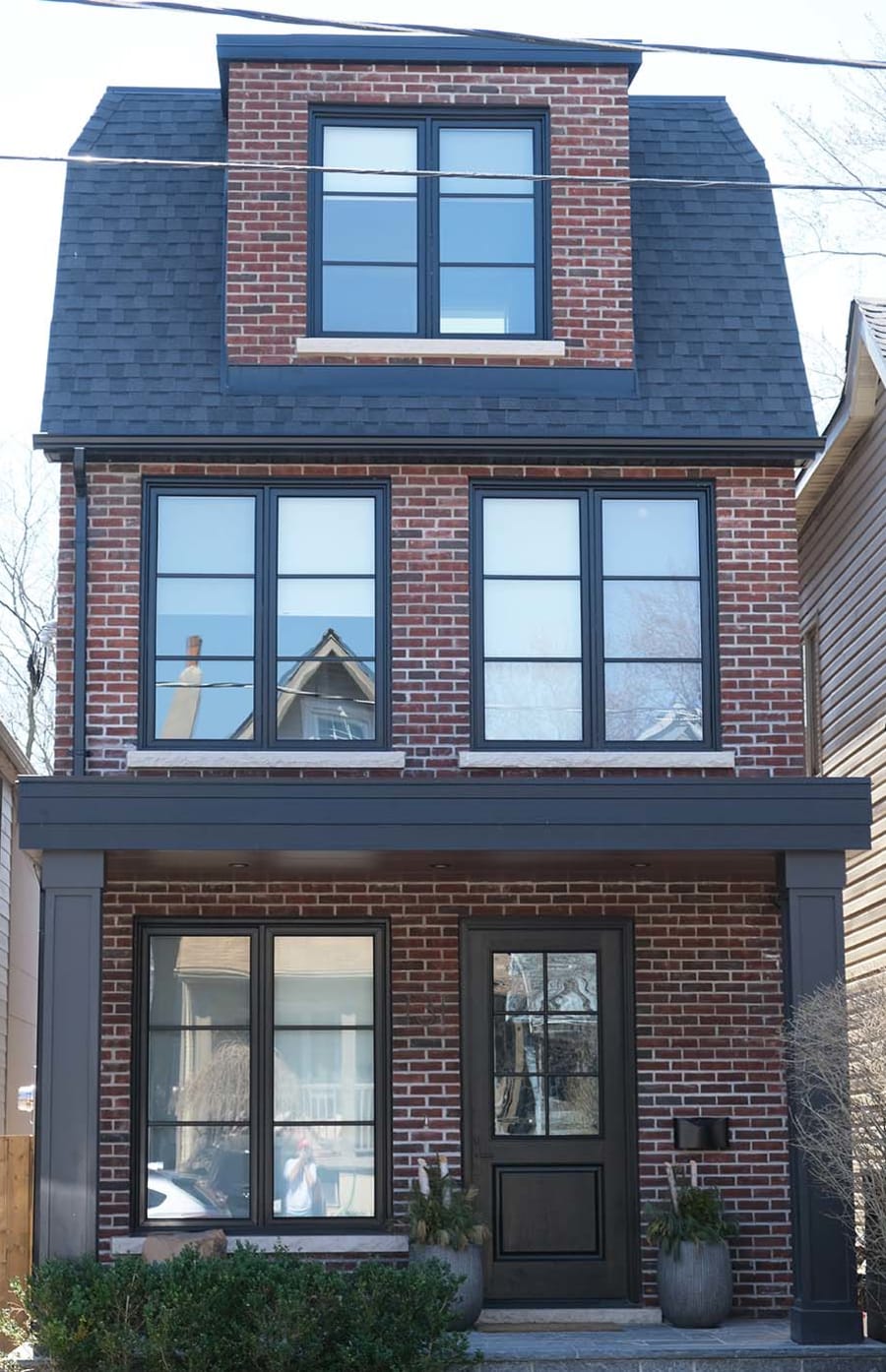 Three story red brick house with brown door and large windows.