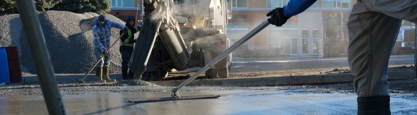 Person's hands wearing rubber gloves levelling wet concrete with a long tool.