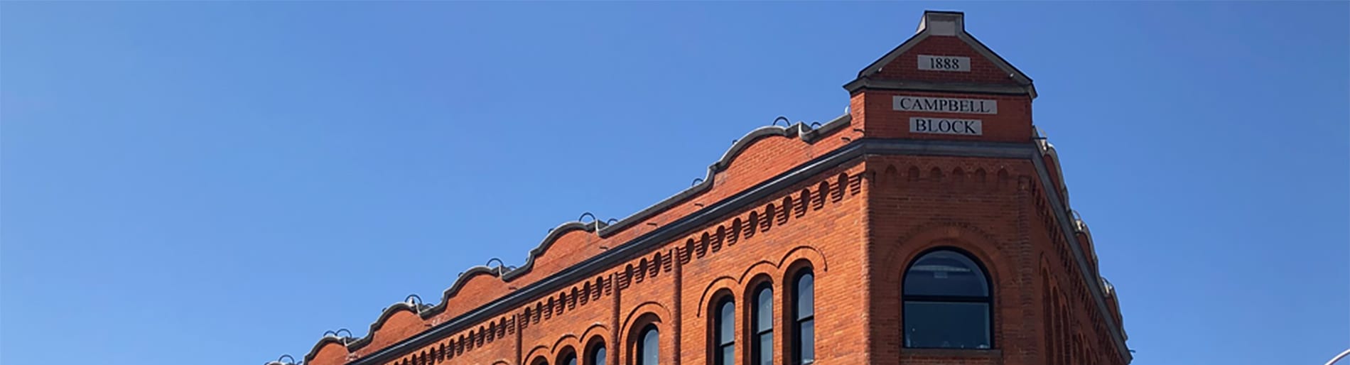 Top of a red brick building with three white signs that say "1888", "Campbell", and "Block" in black text.