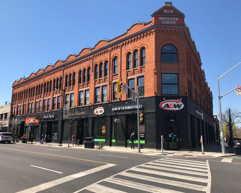 Black and red brick building on a street corner with A&W logo on the exterior.