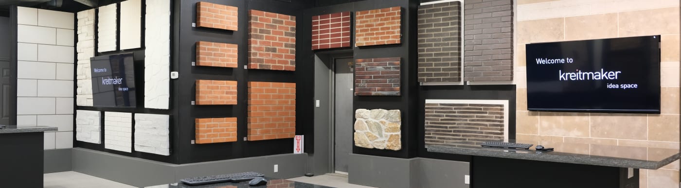 Show room with multiple brick samples in different colours and sizes on the wall and two TV screens, both displaying the [SITE][COMPANY-NAME] logo.