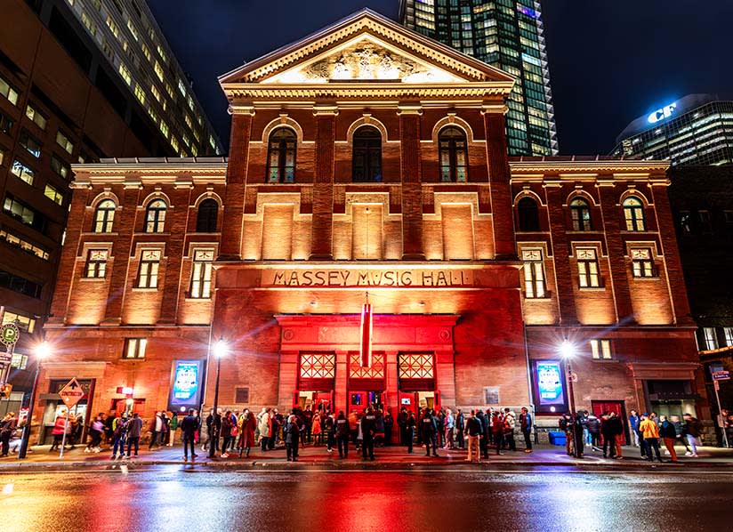 Exterior of Massey Music Hall at night with bright red lights and a crowd of people in front.