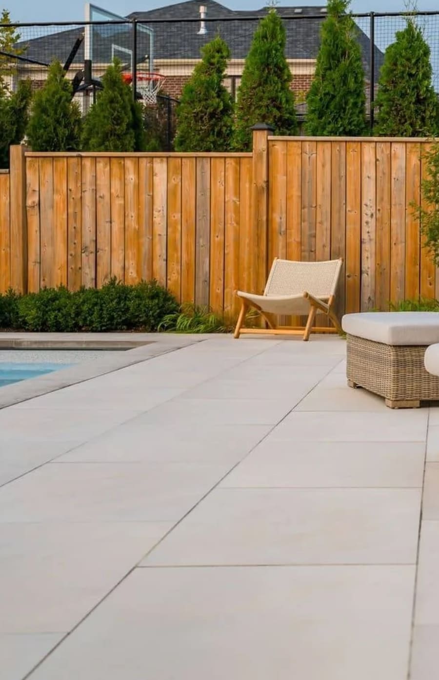 Edge of a pool deck with large beige flagstones and wicker chairs. 