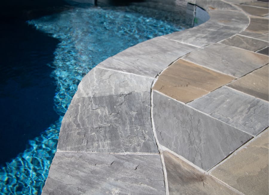 Edge of a pool with grey pavers and flagstone.