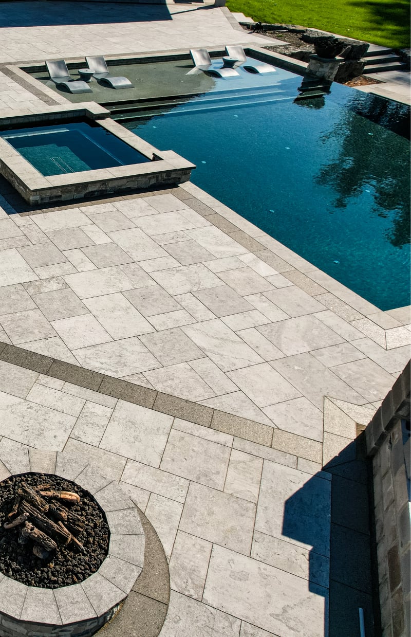 Edge of a pool and hot tub with grey pavers and flagstone.