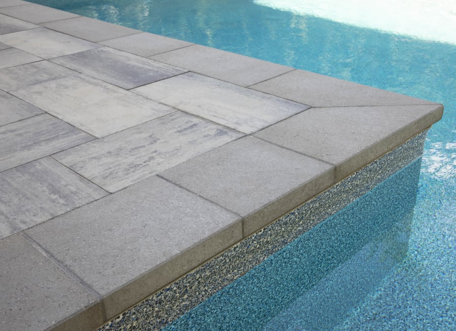 Edge of a pool with grey pavers and flagstone.