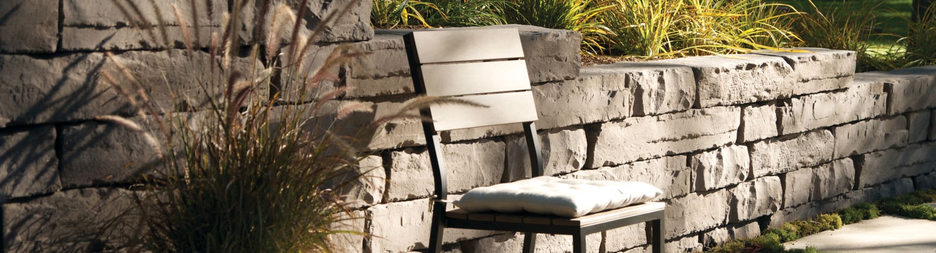 Patio chair sitting in from of stone wall with foliage.