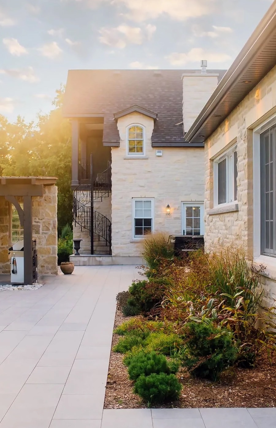 Exterior courtyard of a house with light beige stone, a large patio with garden and a spiral staircase.