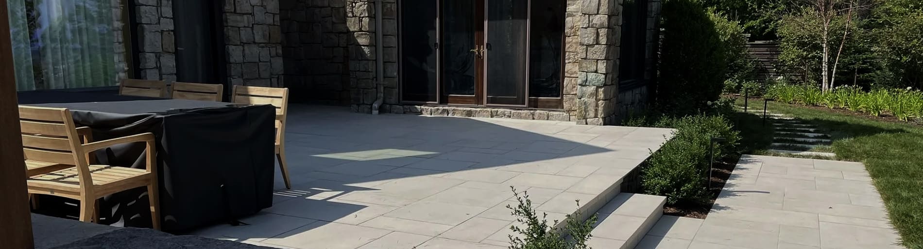 Patio table with chairs sitting on a raised stone patio with a stone path leading to a lawn.