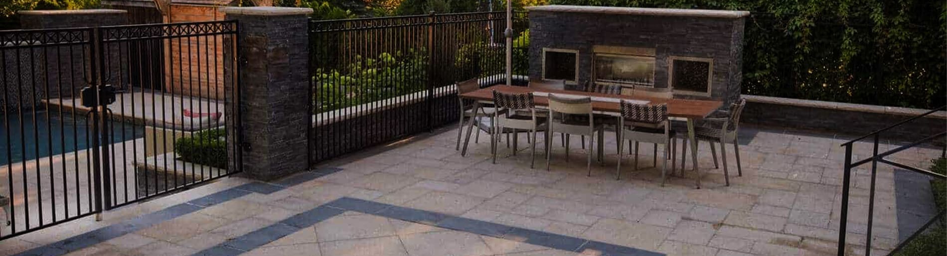 Stone patio and an outdoor dining table sitting in front of a fireplace with wrought iron fence on the left.