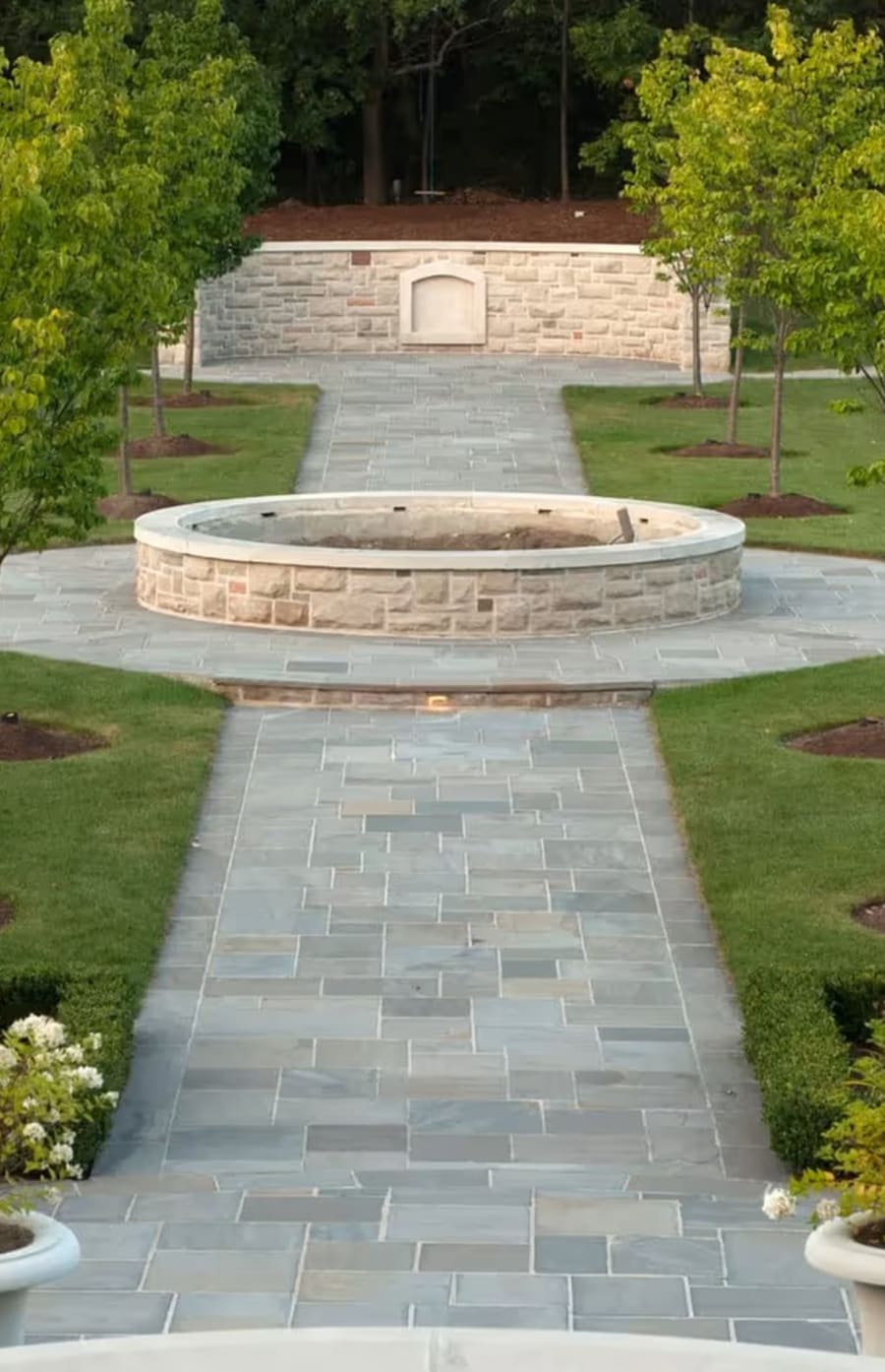 park with a long and wide walkway made of flagstone, in the middle a raised garden bed with stone wall