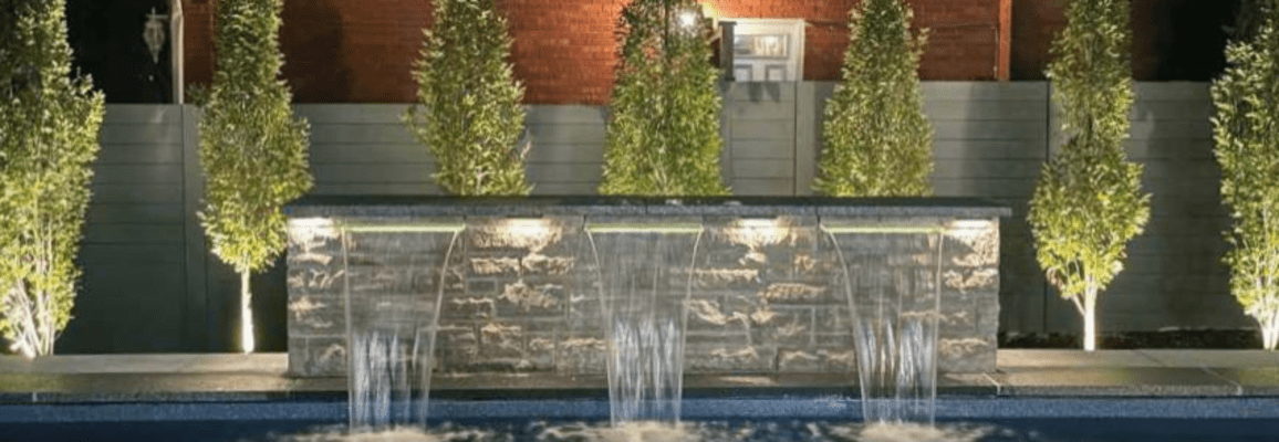 decorative stone wall with 3 fountains pouring into an outdoor pool