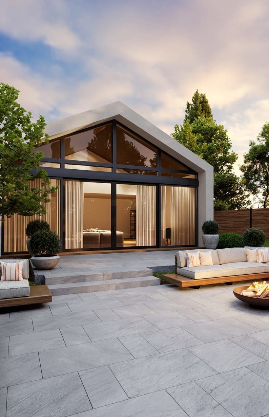 Backyard patio with light grey pavers and an outdoor fire pit with couches.