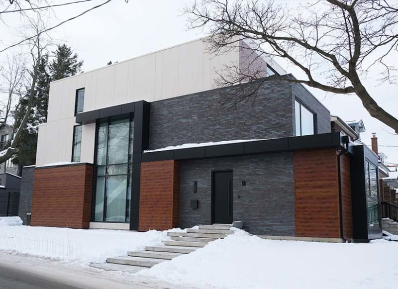 Exterior of a modern house in the winter, with grey brick, wood and light beige siding.