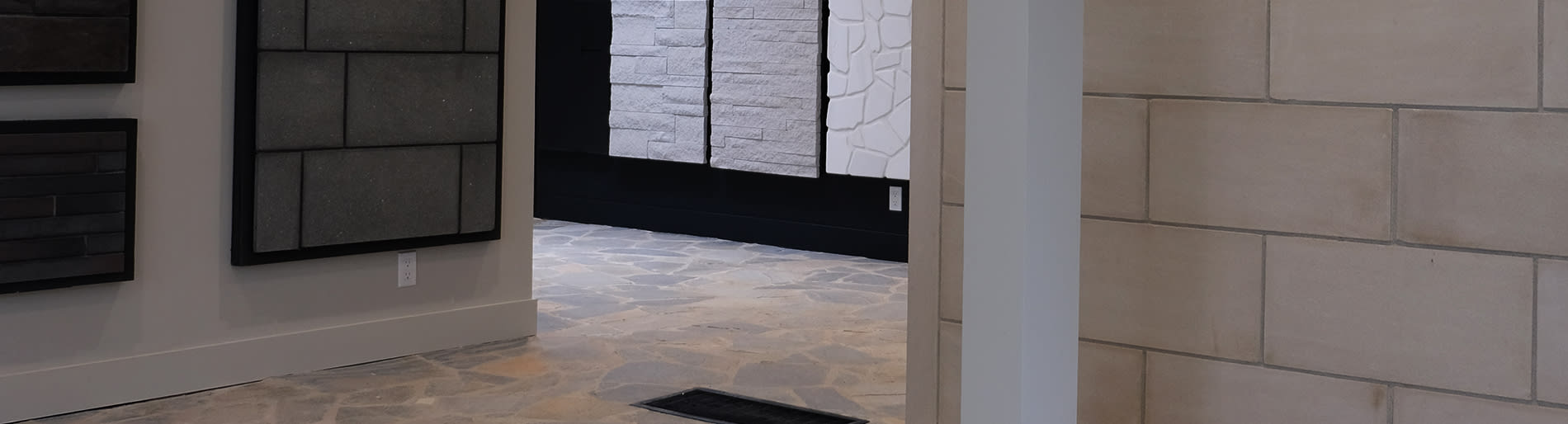 A hallway with a stone floor and stone wall on the right with multiple stone samples hanging on the wall on the left.