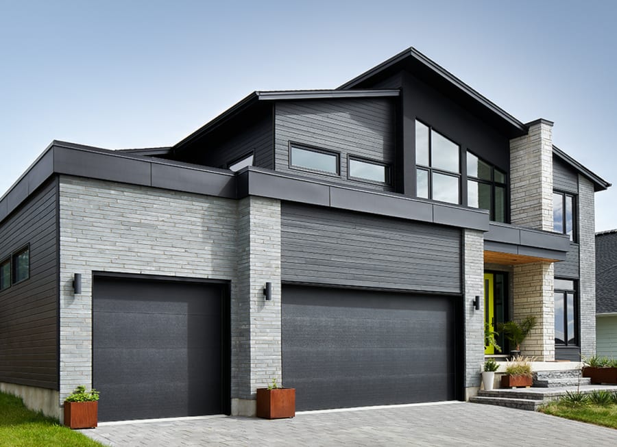 Two story house with grey wall stone and two garage doors.