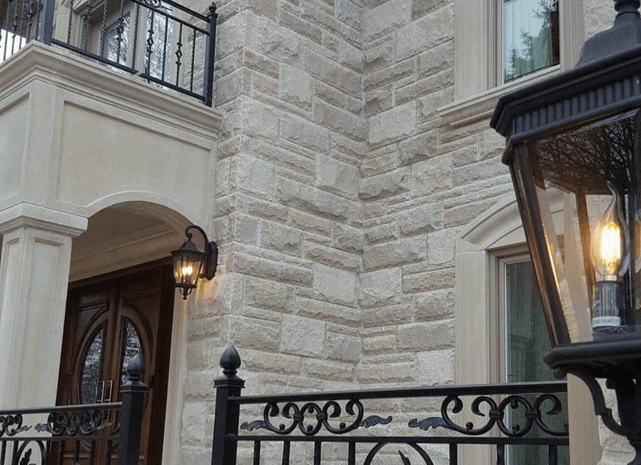 Light beige exterior stone wall with a brown wooden door and iron fence.