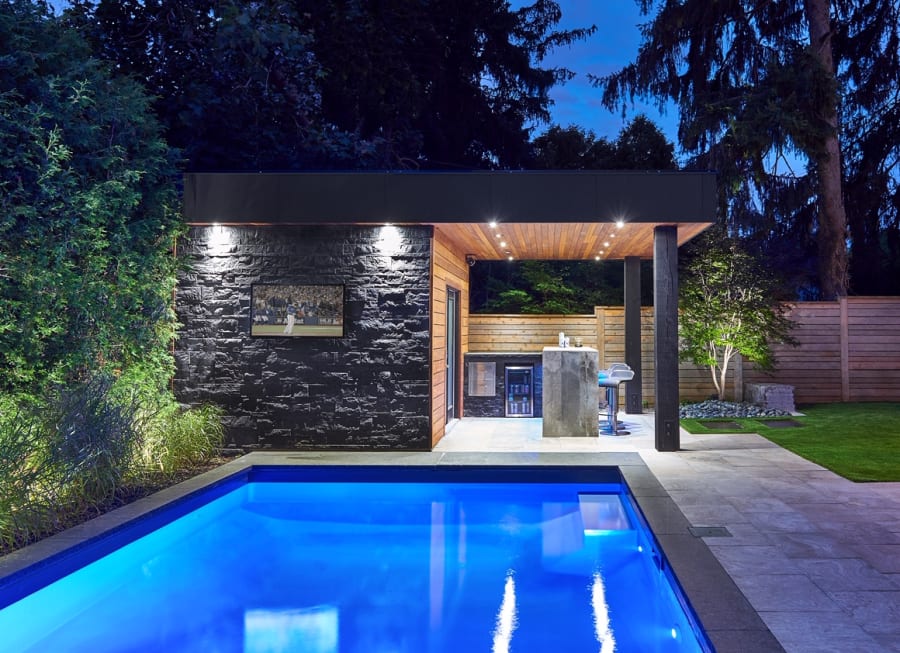 Back yard of a dark grey house with a pool.