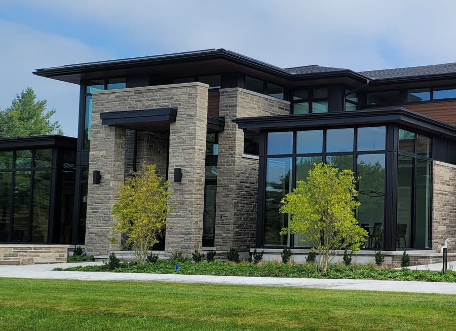 Exterior of a moder home with grey wall stone pillars and large windows.