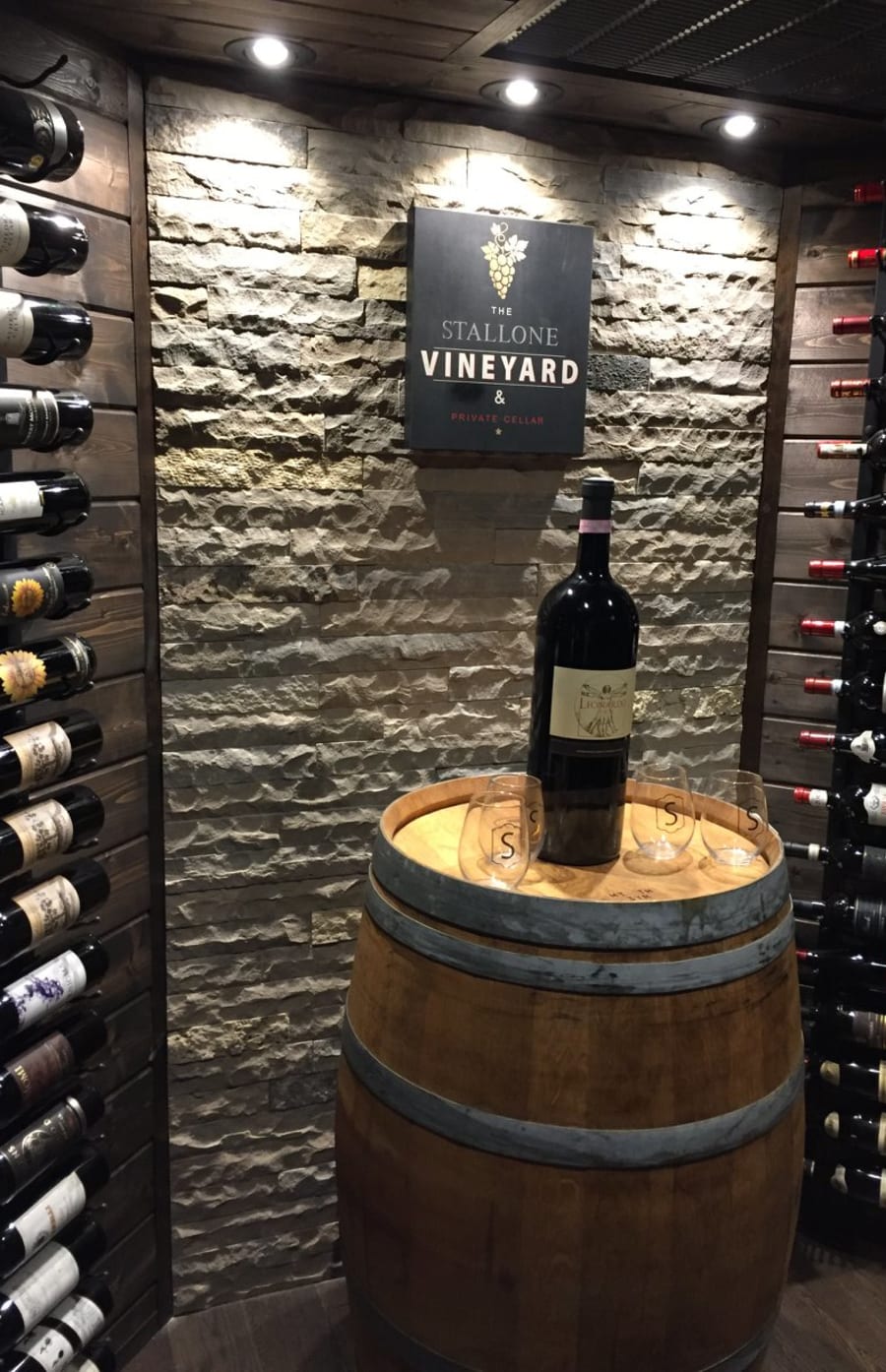 Interior wall of a Vineyard with light grey wall stone surrounded by wine bottles and a barrel.