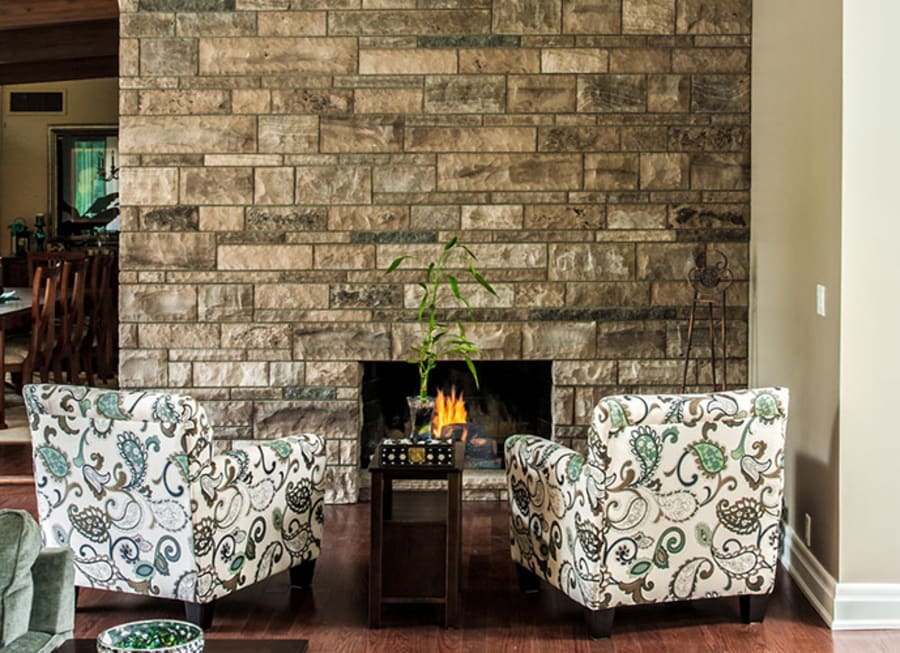 Interior fireplace with beige wall stone and two chairs facing the fireplace.