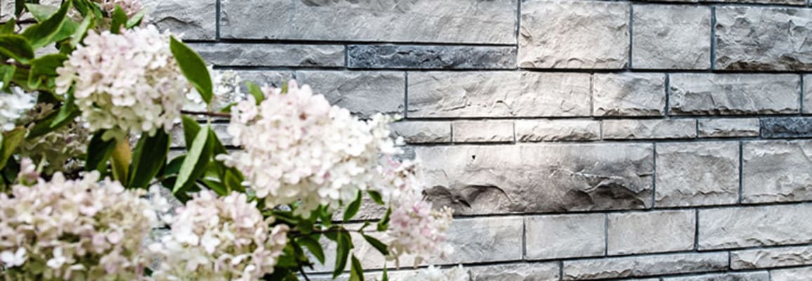 Exterior wall with light grey wall stone with light pink flowers in front of it.