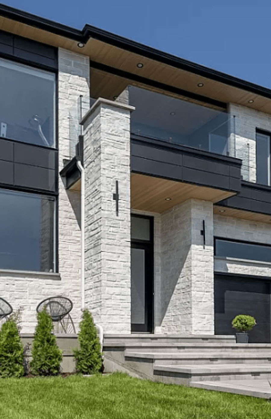 Exterior of a two story house with light grey flagstone walls and pillars.