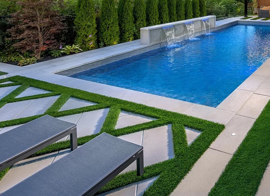 Pool patio with light grey pavers and flagstone with two lounge chairs and grass patterns. 